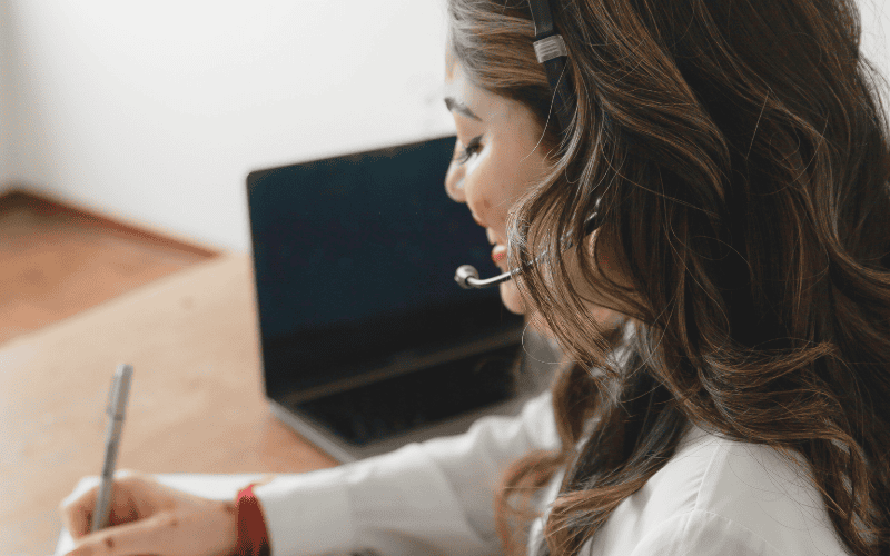 Side profile of a virtual assistant wearing a headset and taking notes, providing customer service.