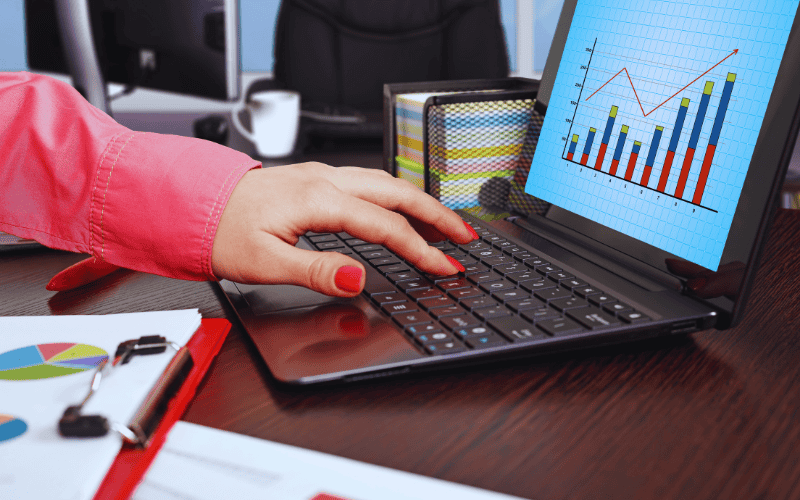A close-up of a virtual assistant's hands typing on a laptop, with a business growth chart on the screen.
