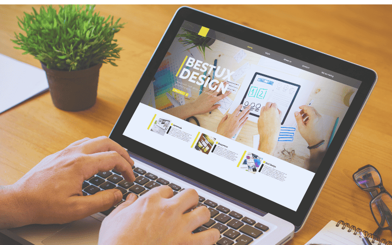Hands typing on a laptop keyboard, with the screen showing a high-quality website template with the text "BEST UX DESIGN.