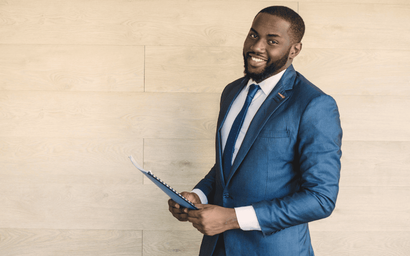 A confident and smiling businessman in a blue suit holding a portfolio.