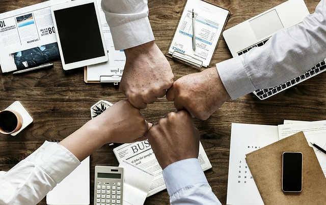 Four fists bumping over a desk filled with business documents, a laptop, and a calculator, symbolizing teamwork and collaboration.
