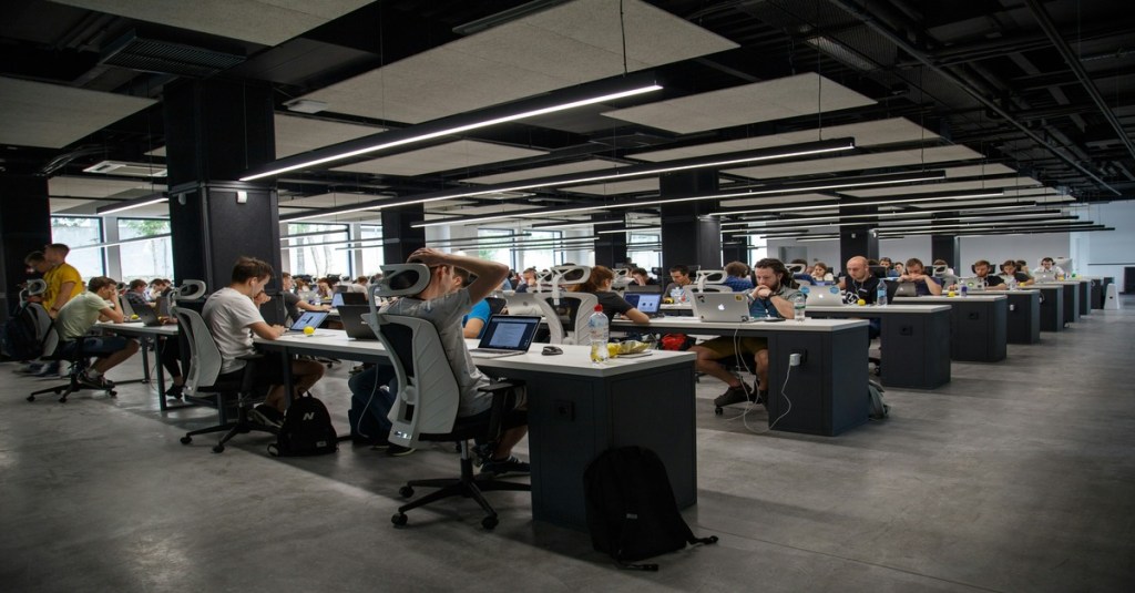 Employees working on laptops in a modern open office, symbolizing 9–5 professionals exploring virtual assistant freelancing side hustles.