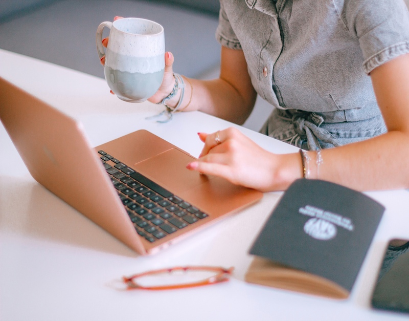 Woman holding a mug and focusing intently on a laptop keyboard at a clean, well-lit desk.